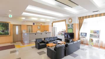 A hotel lobby with a reception desk, seating area, television, and a bulletin board.