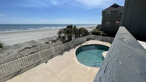 A swimming pool with a wooden deck, a beach view, and a building in the background. - Surfside Landing 101 - Oceanfront in Surfside Beach (Surfside Beach)