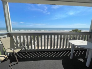 A balcony with a view of the beach, a table, and two chairs.