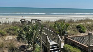 A beach view with a wooden staircase leading to a building, surrounded by vegetation. - Surfwatch II 202 - Oceanfront in Surfside Beach (Surfside Beach)