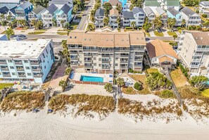 A beachfront hotel with multiple balconies, a swimming pool, and a beach access path.