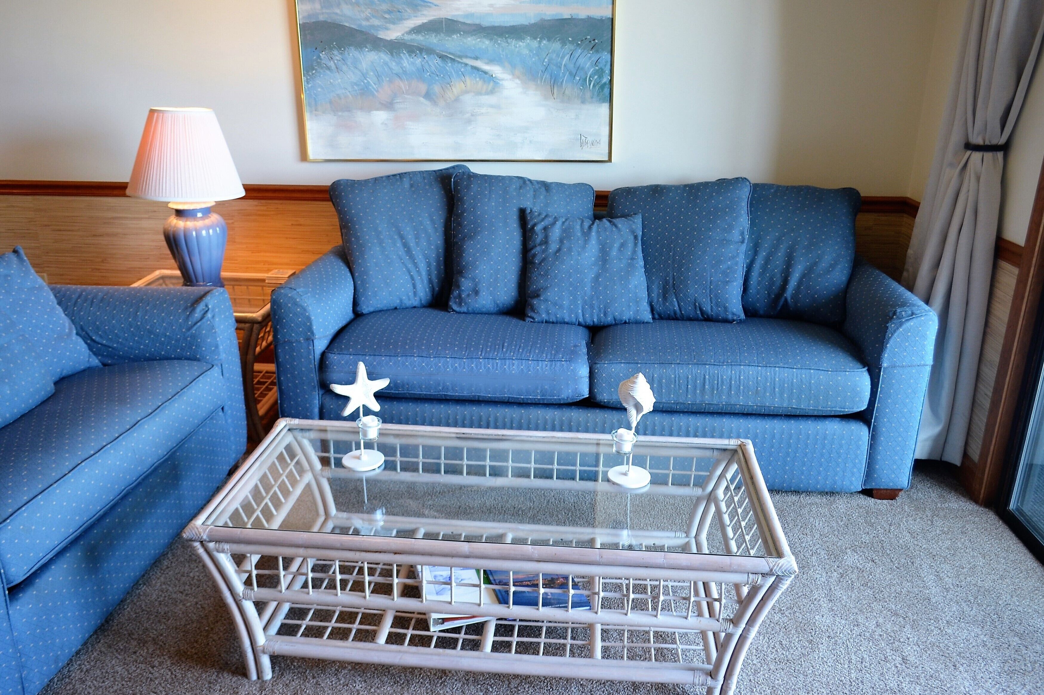 A blue sofa with star-shaped decorations, a glass coffee table, and a lamp.