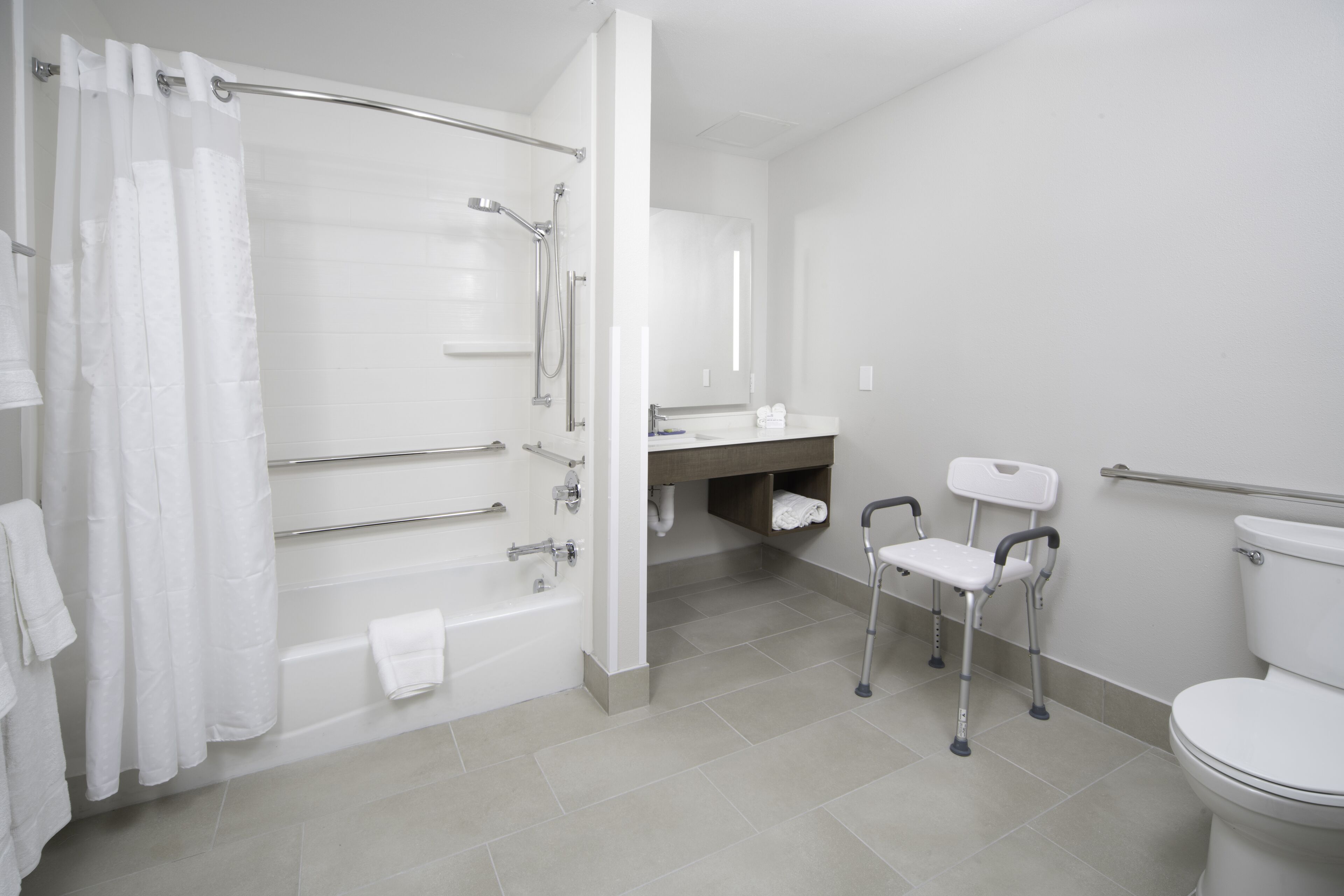 A modern bathroom with a bathtub, shower, toilet, and a handrail for accessibility.