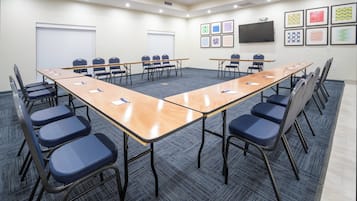 Un salón de conferencias con una larga mesa, sillas y una pantalla de proyector.