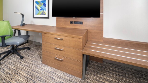 A modern office desk with a flat-screen monitor, a green chair, and a wooden cabinet with drawers. - Holiday Inn Express & Suites Fort Myers Airport by IHG (Fort Myers)