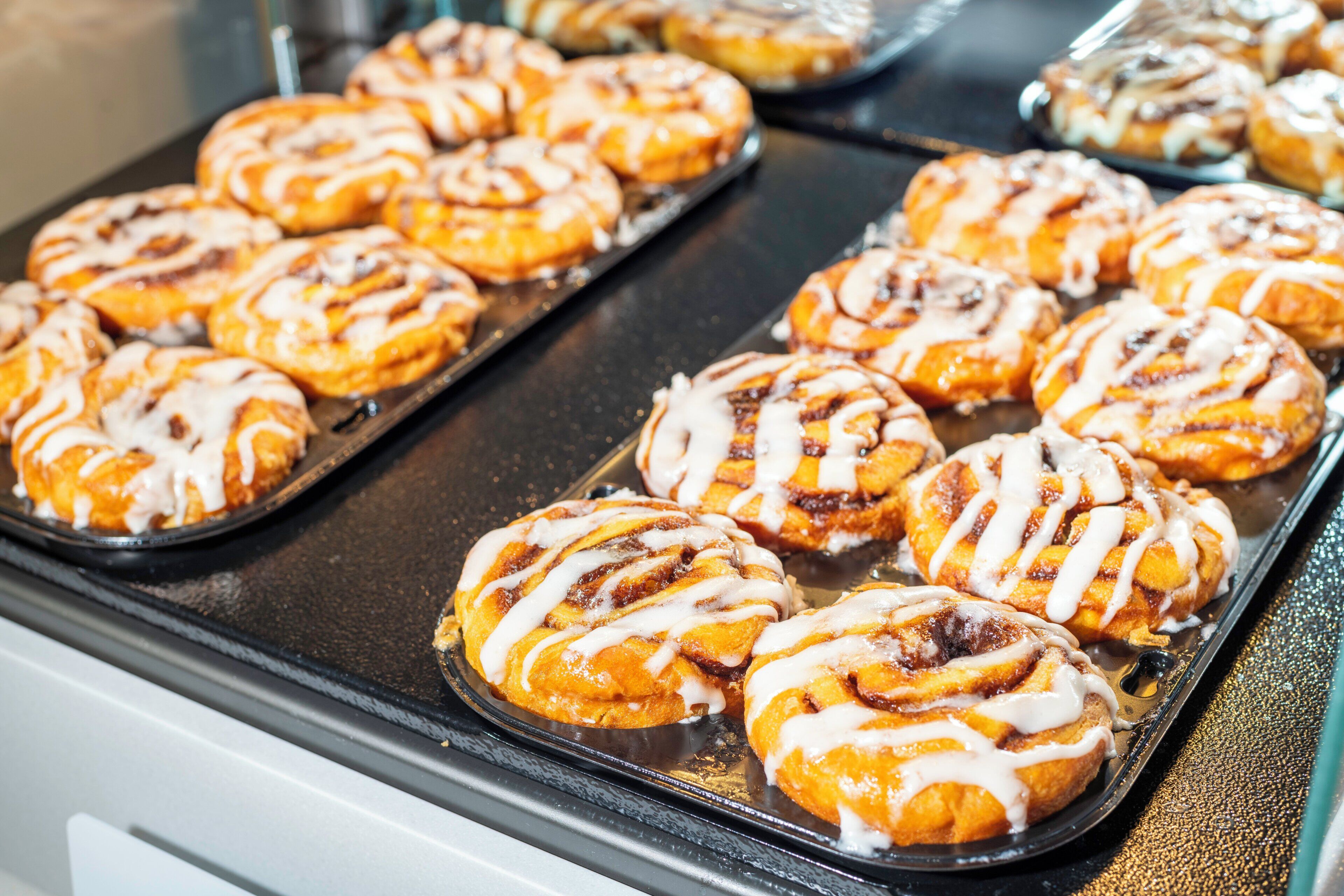 Une plaque de viennoiseries à la cannelle, recouvertes de glaçage, posée sur une surface métallique.
