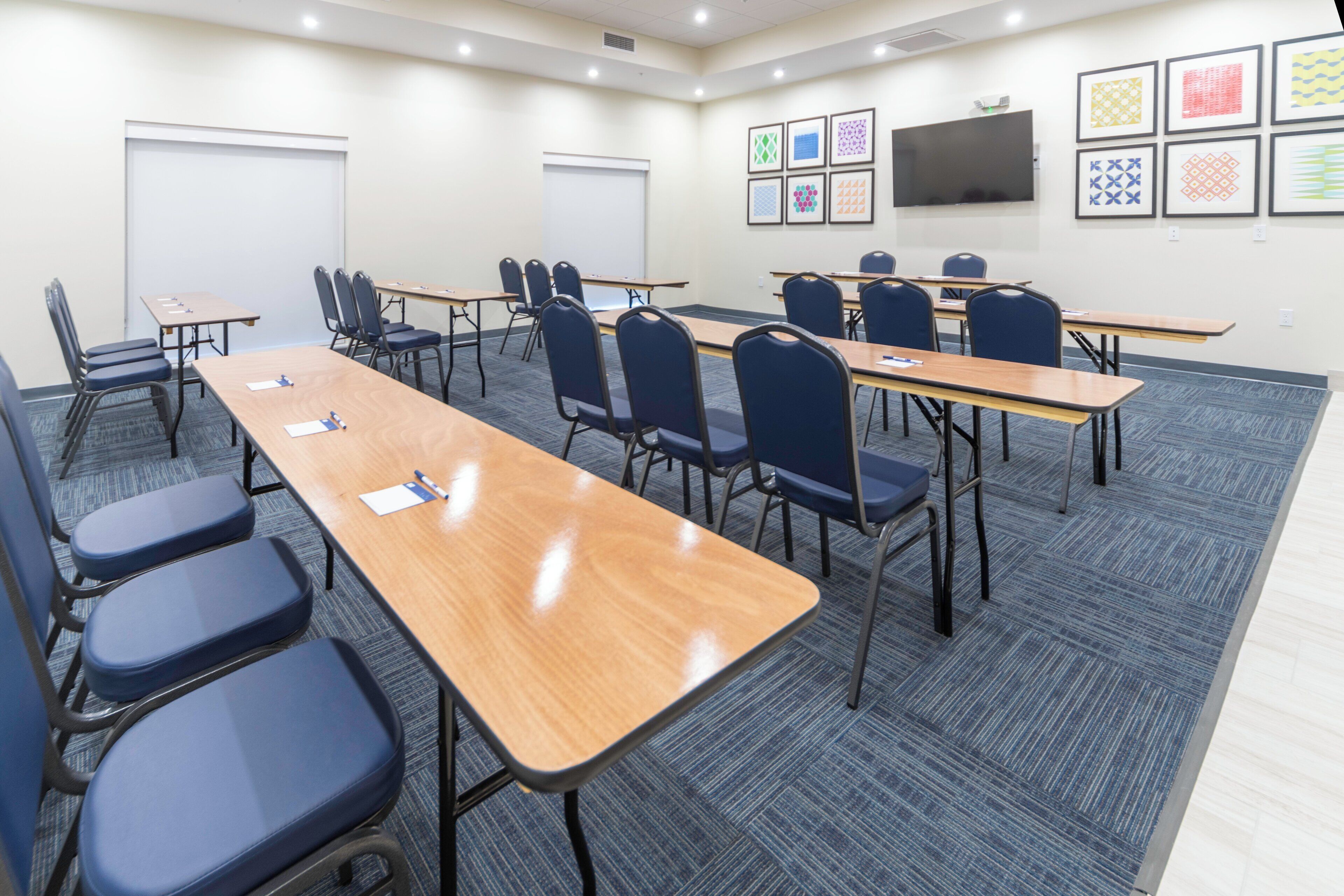 A conference room with multiple tables and chairs, a whiteboard, and a flat-screen TV mounted on the wall.