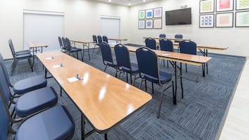 A conference room with multiple tables and chairs, a whiteboard, and a flat-screen TV mounted on the wall.