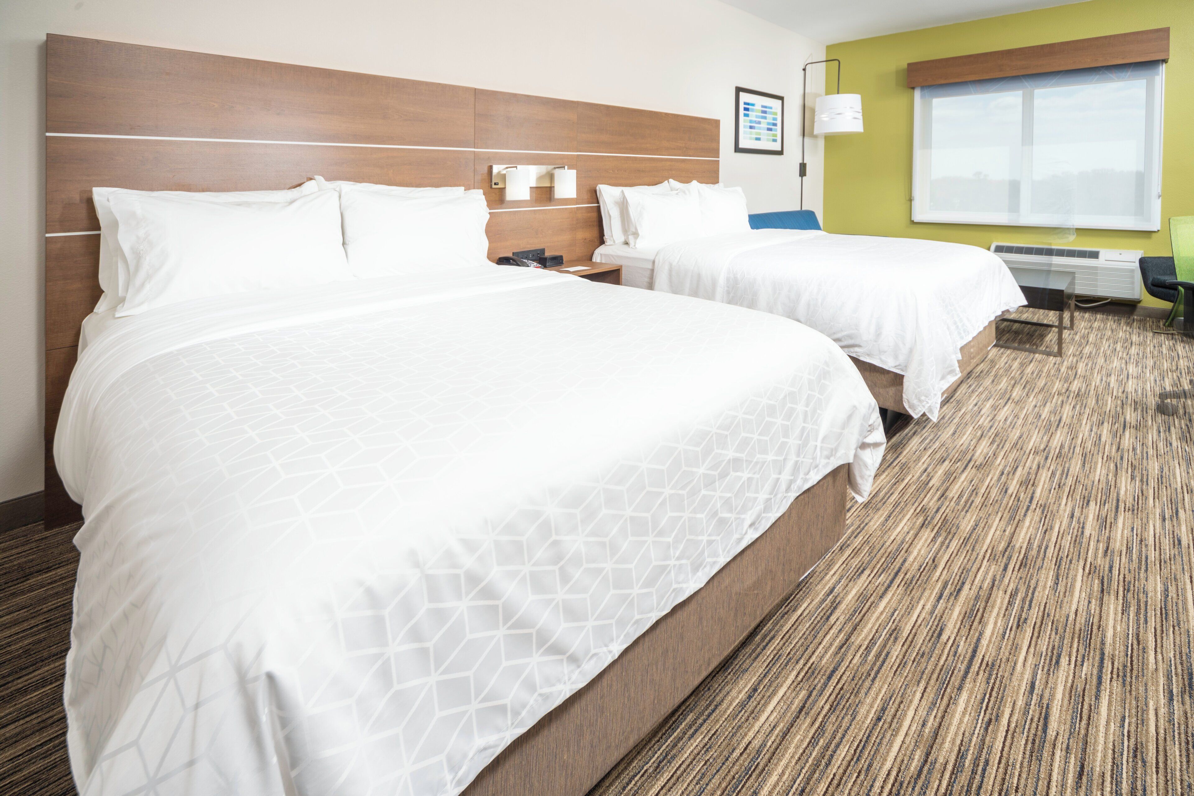 A hotel room with two beds, a desk, and a window.