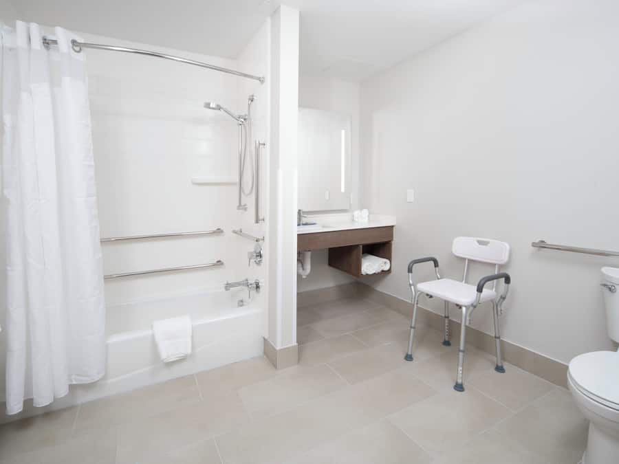 Casa de banho com banheira, chuveiro, sanita e um banco acessível para cadeiras de rodas.