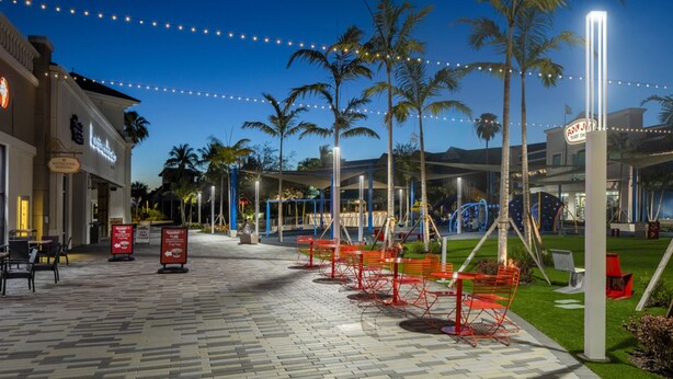 Un espacio al aire libre empedrado con palmeras, luces colgantes y mobiliario exterior.