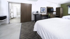 Habitación de hotel con cama, escritorio, silla, televisión y baño visible a través de una puerta abierta.