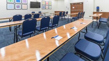 A conference room with long tables and blue chairs, a TV on the wall, and framed artwork on the walls.