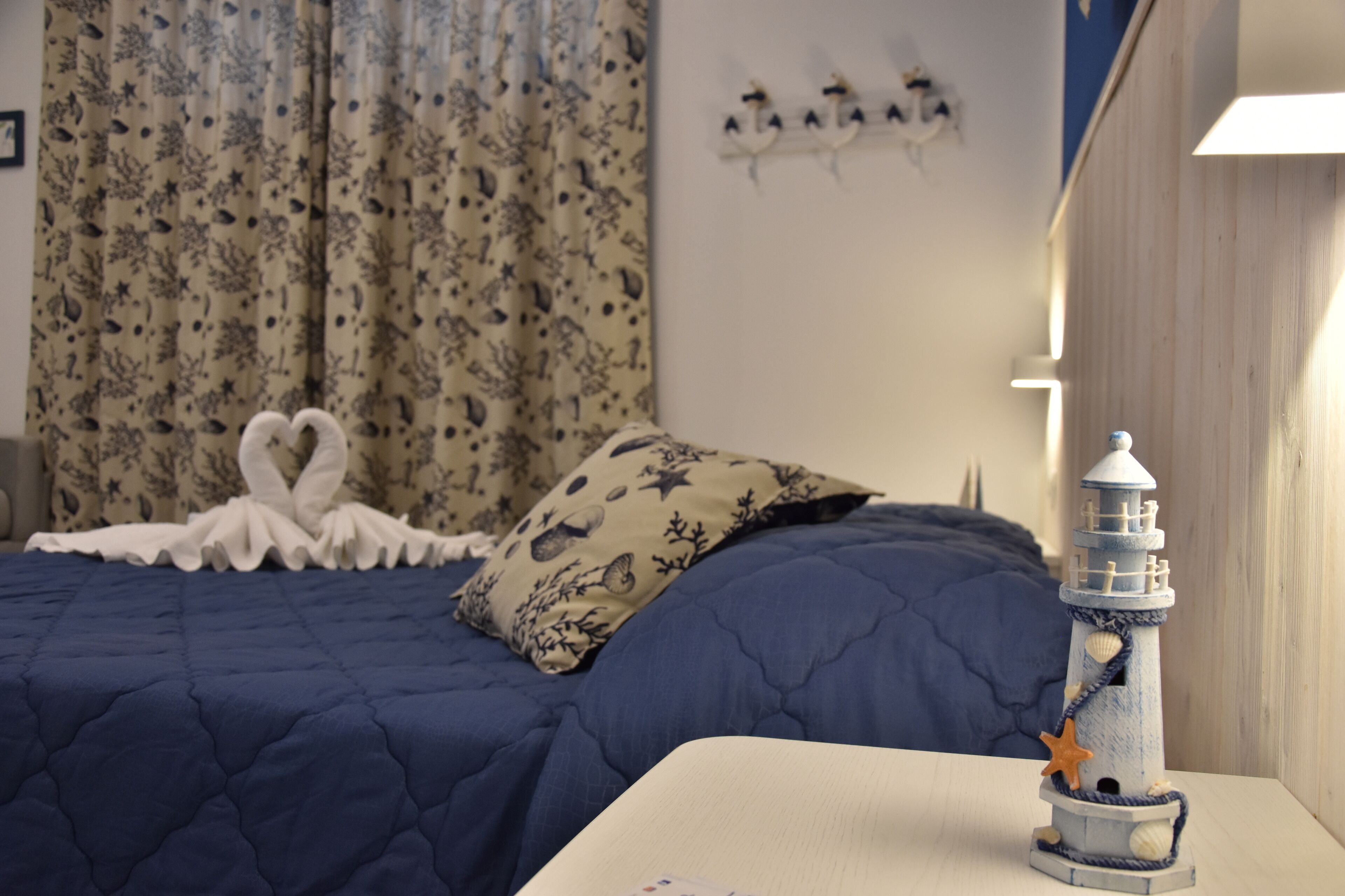 Una cama bien hecha con un edredón azul, un cojín decorativo y un pequeño adorno de faro sobre una mesita de noche.