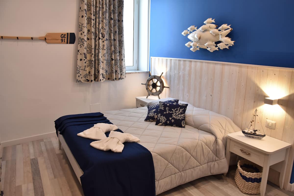 A bedroom with a bed, a nightstand, a wall clock, and a window with curtains.
