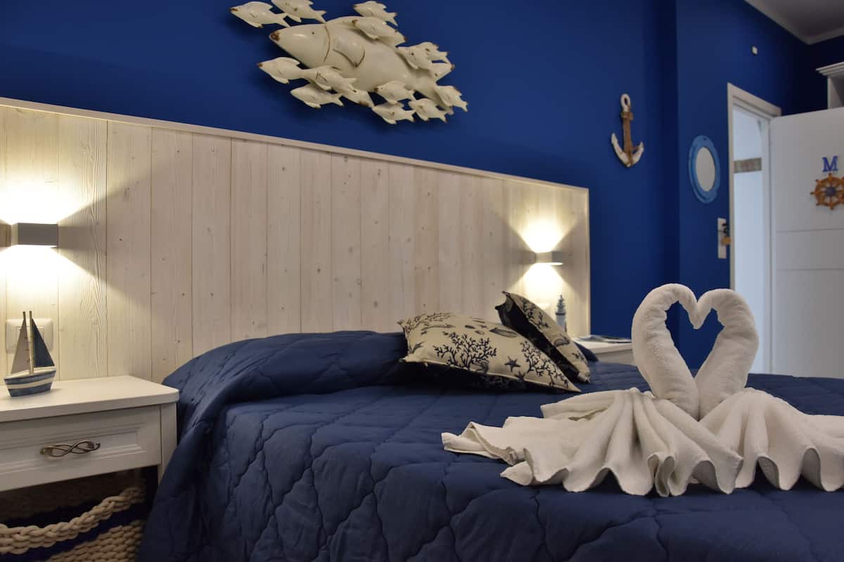 A bedroom with a blue bedspread, a wooden headboard, and a decorative wall piece.