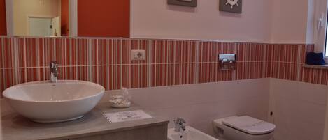 Un baño con un lavamanos grande de color blanco, dos inodoros y un bidé.