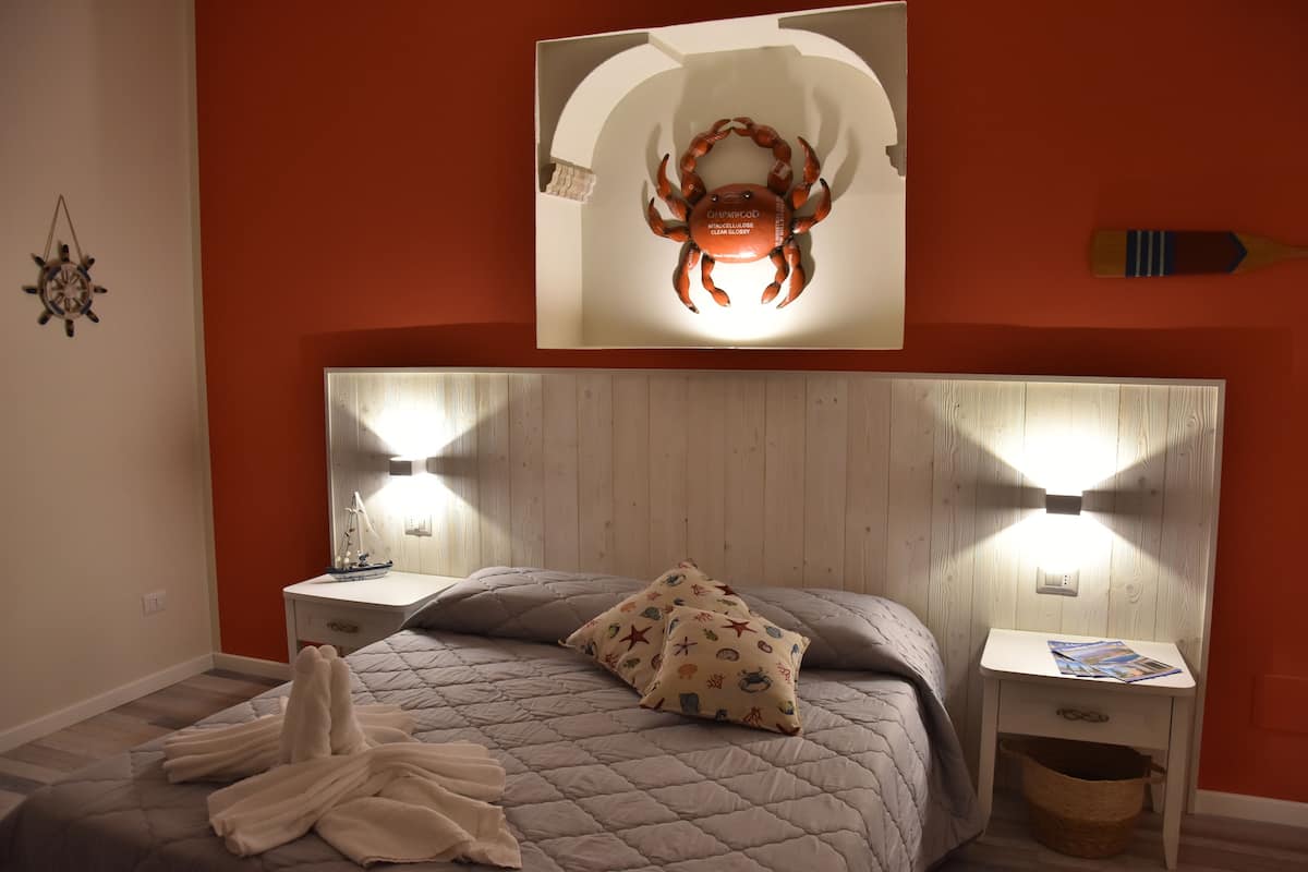 A bedroom with a bed, two bedside tables, a nightstand, a wall-mounted artwork of a crab, and a wall clock.