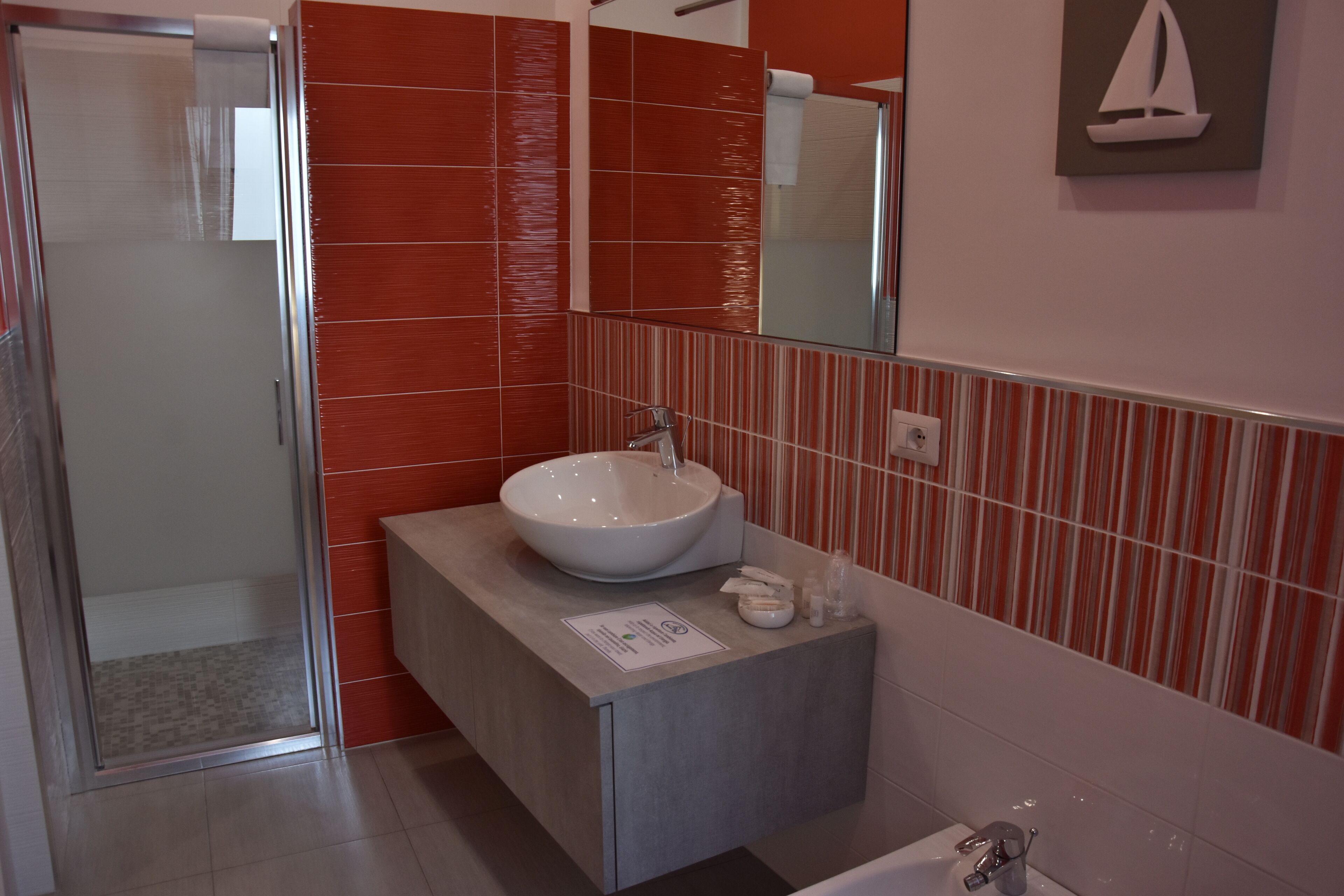Un baño moderno con mampara de vidrio, un lavamanos blanco y pared con azulejos a rayas.