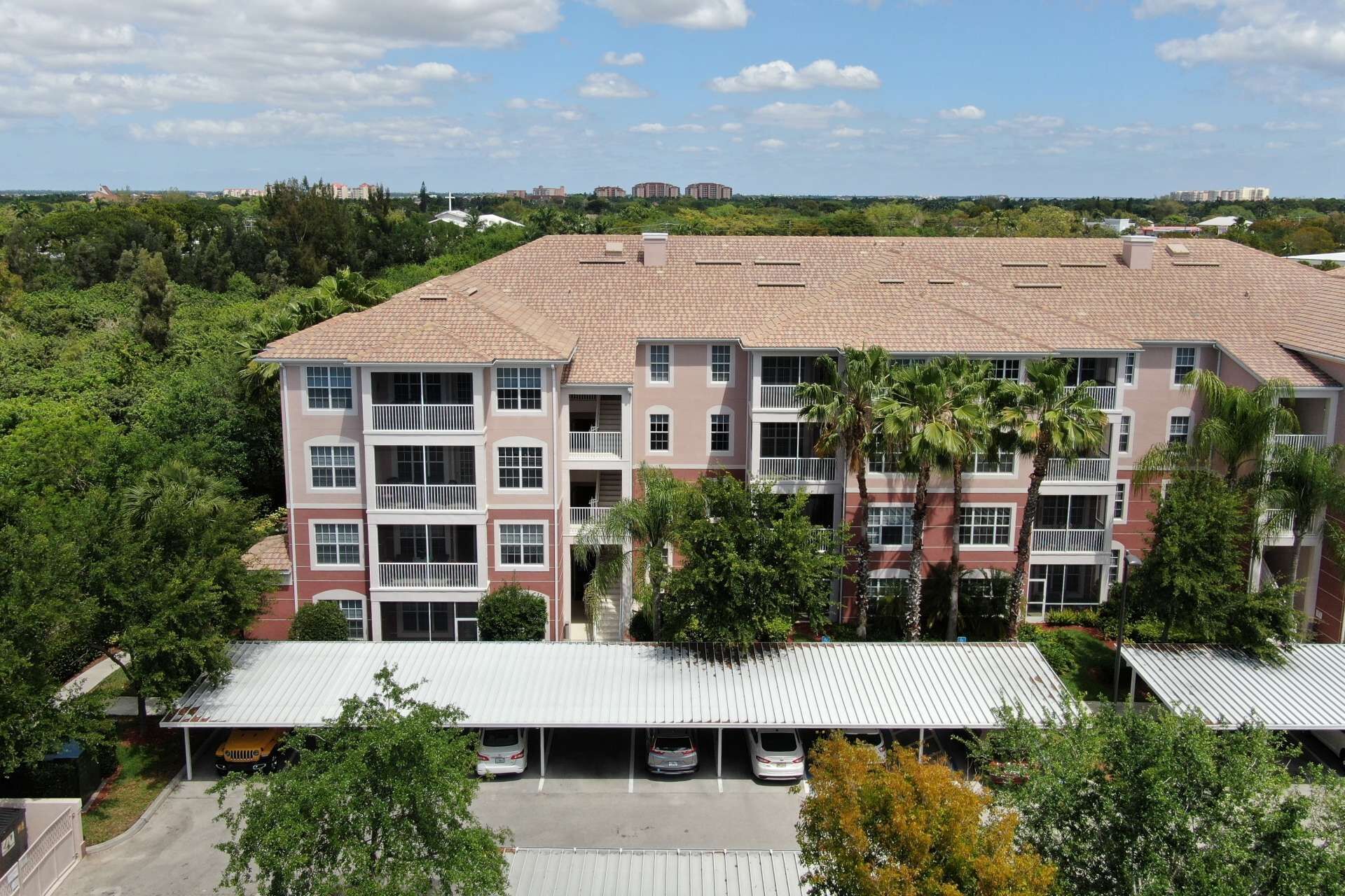 A multi-story residential building with a flat roof, multiple balconies, and a parking area with several cars.