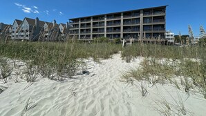 A multi-story hotel with balconies, located near a sandy beach with tall grasses. - Sea Shadow 306 - Oceanfront in Surfside Beach (Surfside Beach)