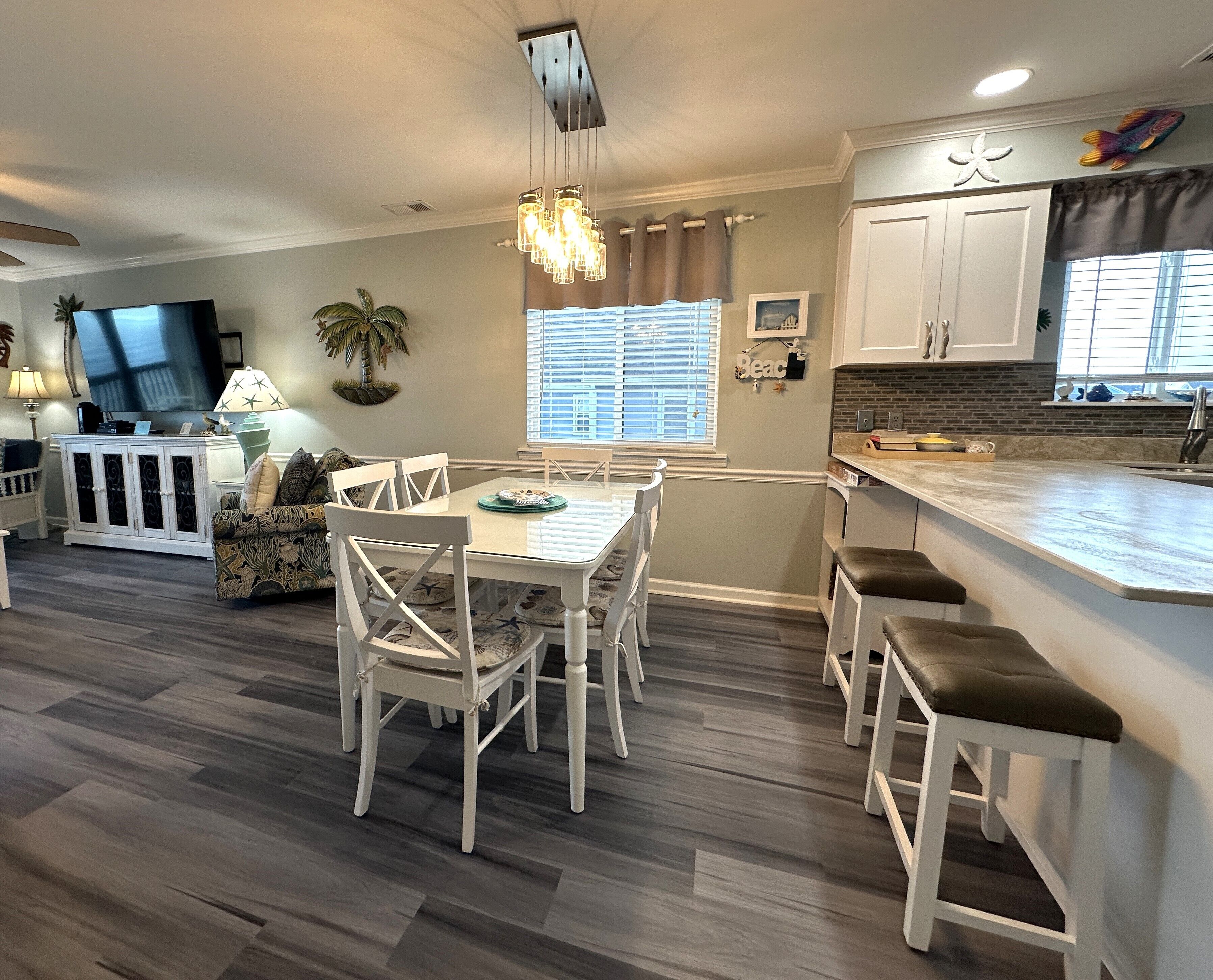 A modern kitchen with white cabinets, a large island with bar stools, a dining area with a table and chairs, and a TV in the living area.