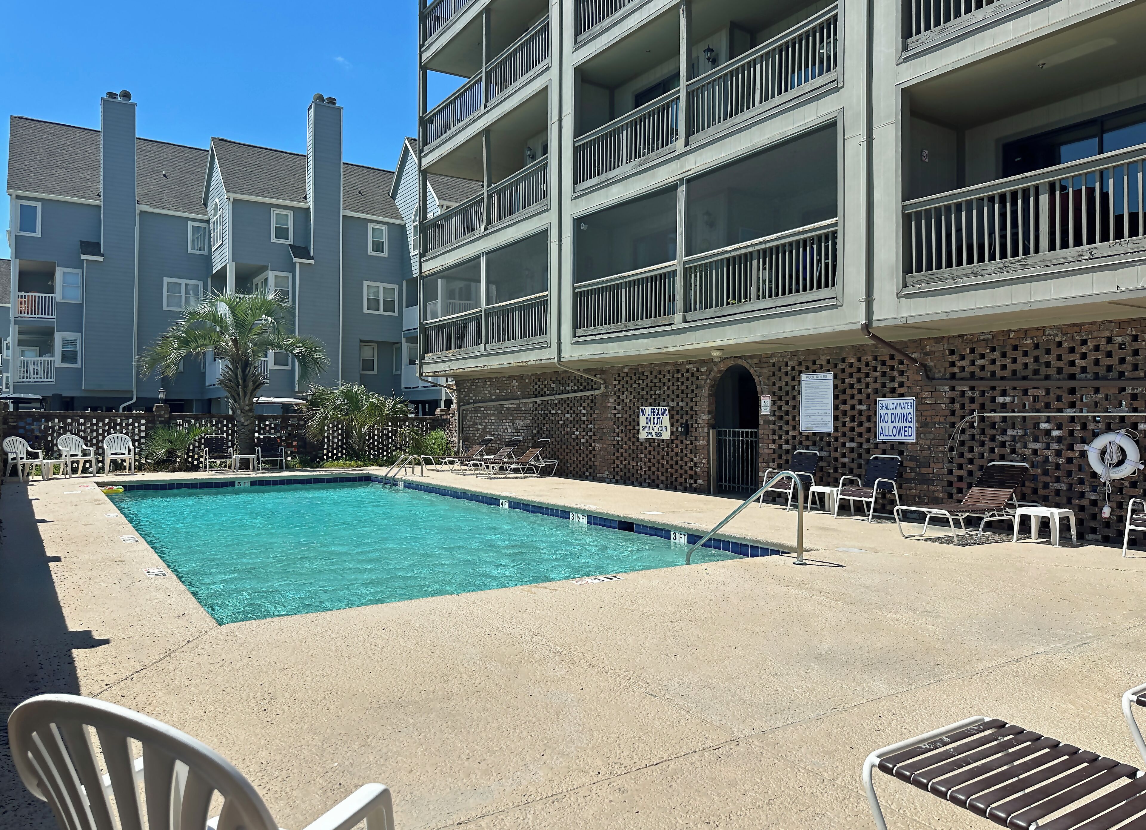 A pool area with lounge chairs and a brick wall with safety signs.