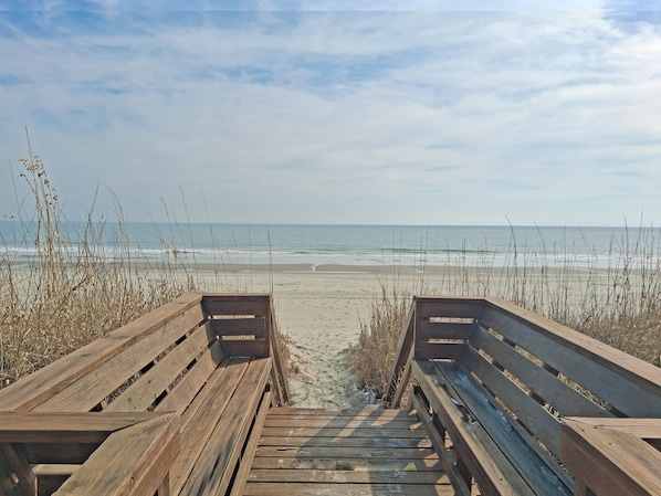 A wooden boardwalk leading to a beach with a clear view of the ocean.