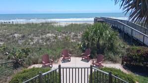 A beach view with a wooden deck, red Adirondack chairs, and a palm tree. - Second Creek - Oceanfront in Garden City Beach (Garden City)