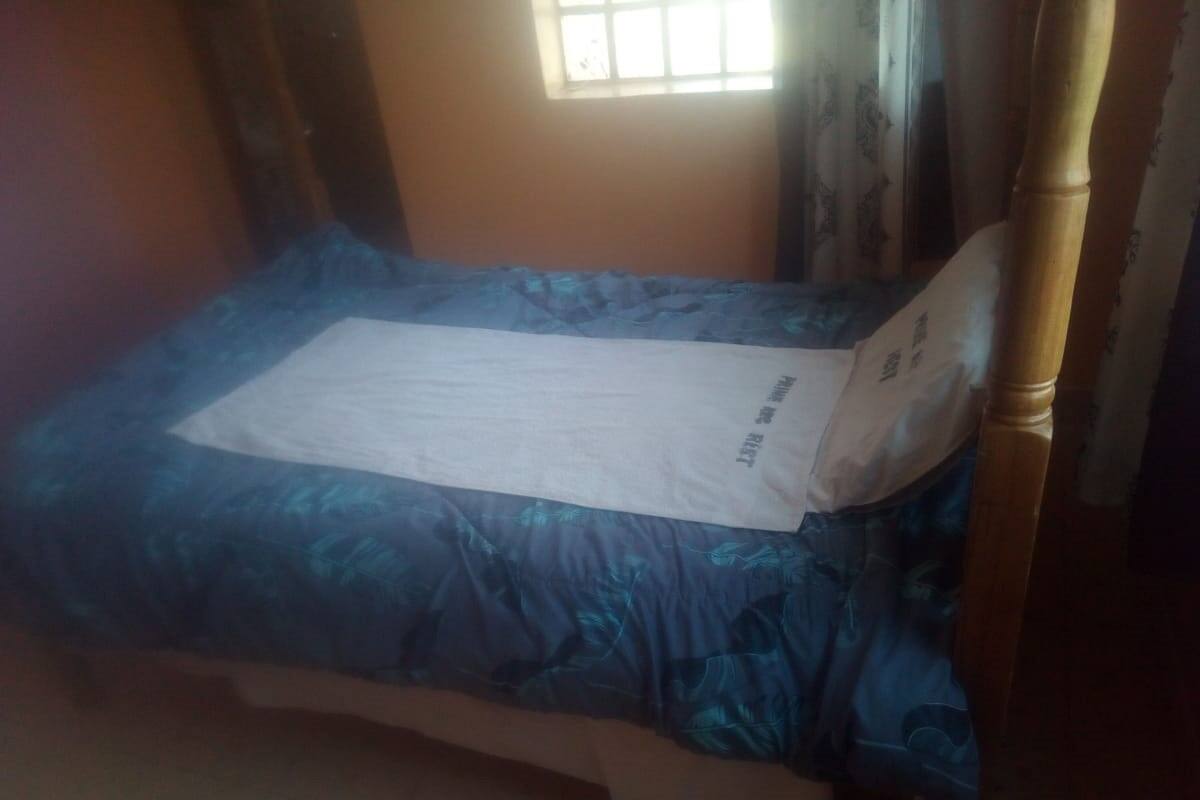 A single bed with a blue patterned bedspread and a white pillow.