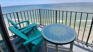 Un balcon avec vue sur l’océan, une table ronde et deux chaises turquoise.