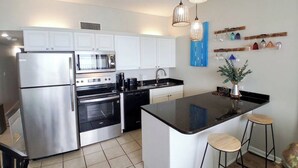 Une cuisine moderne dotée d’appareils électroménagers en acier inoxydable, d’un îlot central, de tabourets de bar, de luminaires suspendus et d’objets décoratifs sur le mur.