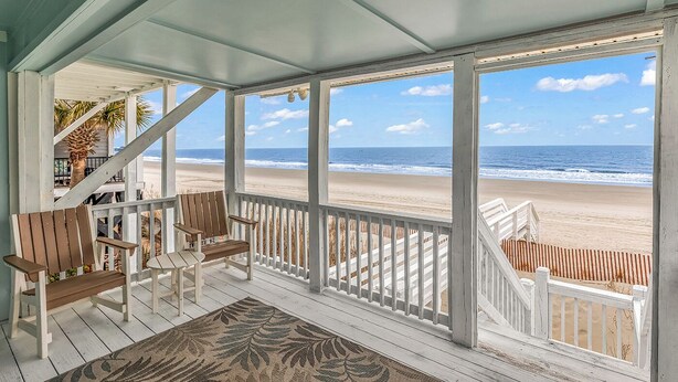 Une véranda donnant sur la plage, avec des chaises en bois et un tapis à motifs.