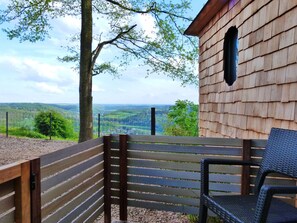 Una terraza de madera con un banco y una silla, con vistas a un valle con cerca y árboles.
