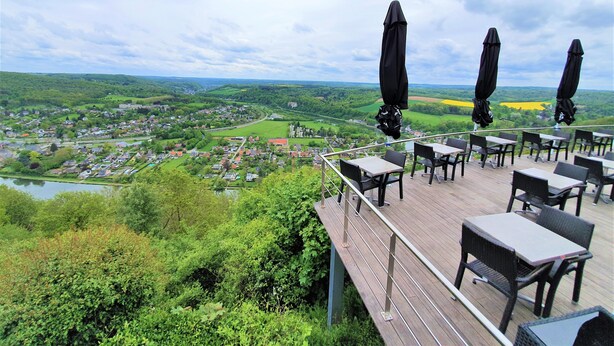 Un área de comedor al aire libre con mesas y sillas, con vistas a un paisaje pintoresco con vegetación y un pueblo abajo.