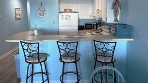 A kitchen with a central island, three bar stools, and a microwave. - Sand Dollar 101 - Oceanfront in Garden City Beach (Garden City)