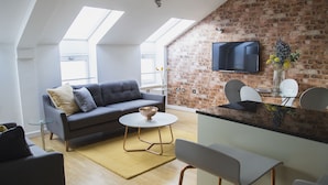 A modern living room with a sofa, a coffee table, and a TV mounted on a brick wall.