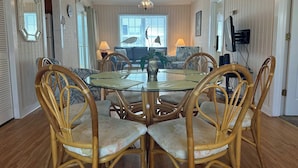 Un coin repas comprenant une table ronde en verre, six chaises en bois dotées de sièges rembourrés et un lustre.