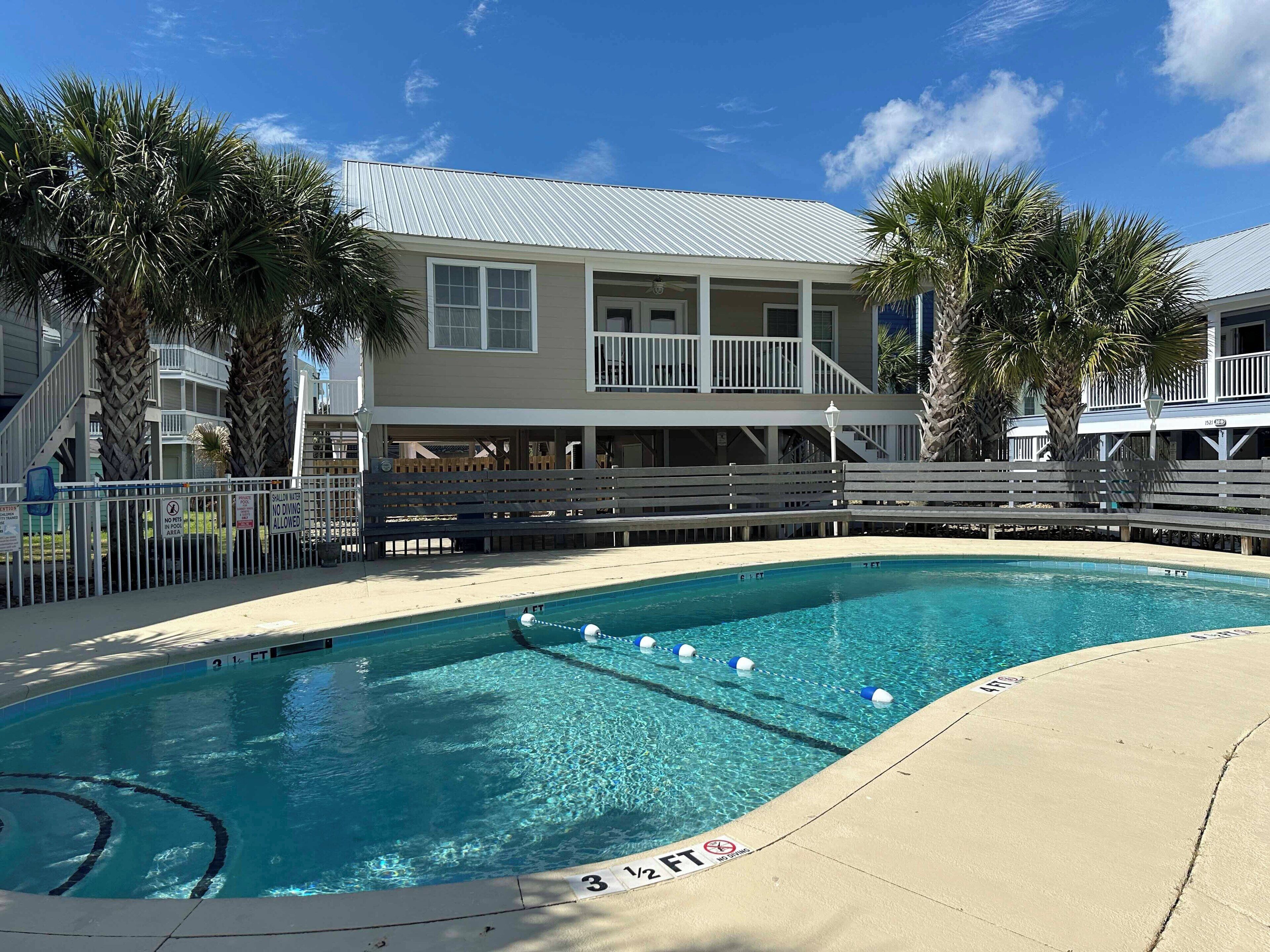 A swimming pool with a deck area, surrounded by a building with a balcony and palm trees.