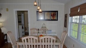 A dining area with a table and chairs, a hanging light fixture, and a window with a view of greenery. - Summer Winds 14 - Second Row Complex in Garden City Beach (Garden City)