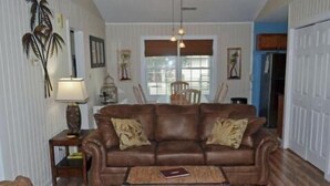 A living room with a brown leather sofa, a small side table, and a woven ottoman. - Summer Winds 14 - Second Row Complex in Garden City Beach (Garden City)