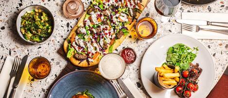 A dining table with various dishes including a burger, pizza, and steak with cherry tomatoes.