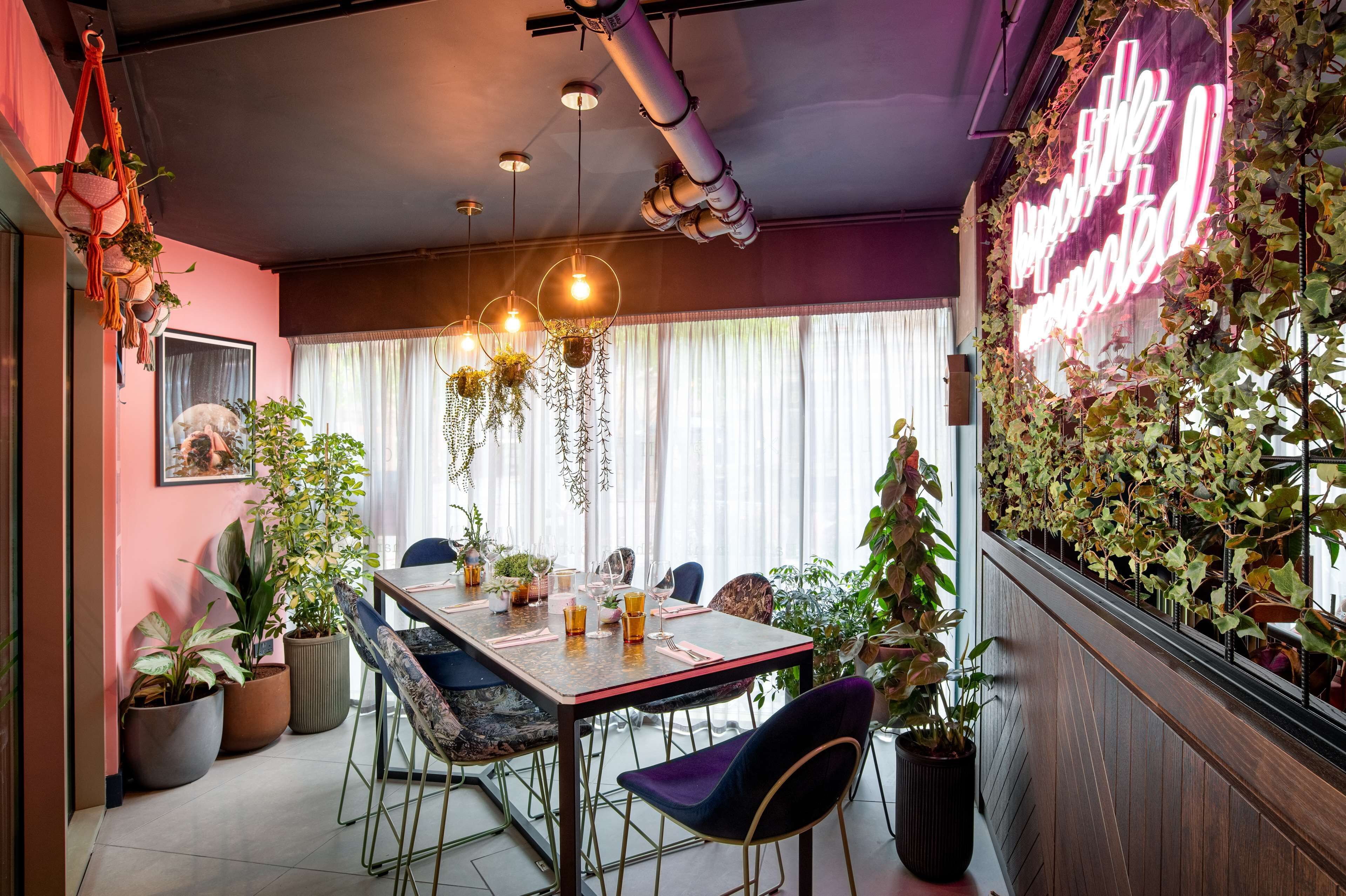 A dining area with a table set for four, surrounded by potted plants and hanging plants.