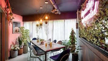Un comedor con una mesa dispuesta para cuatro personas, rodeado de plantas en macetas y plantas colgantes.