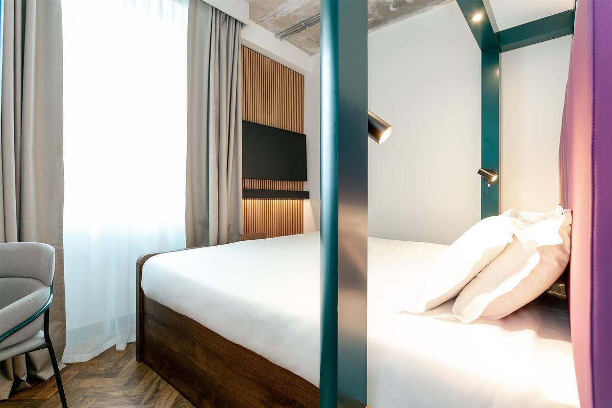 A hotel room with a bed, a chair, a TV, and a window with curtains.