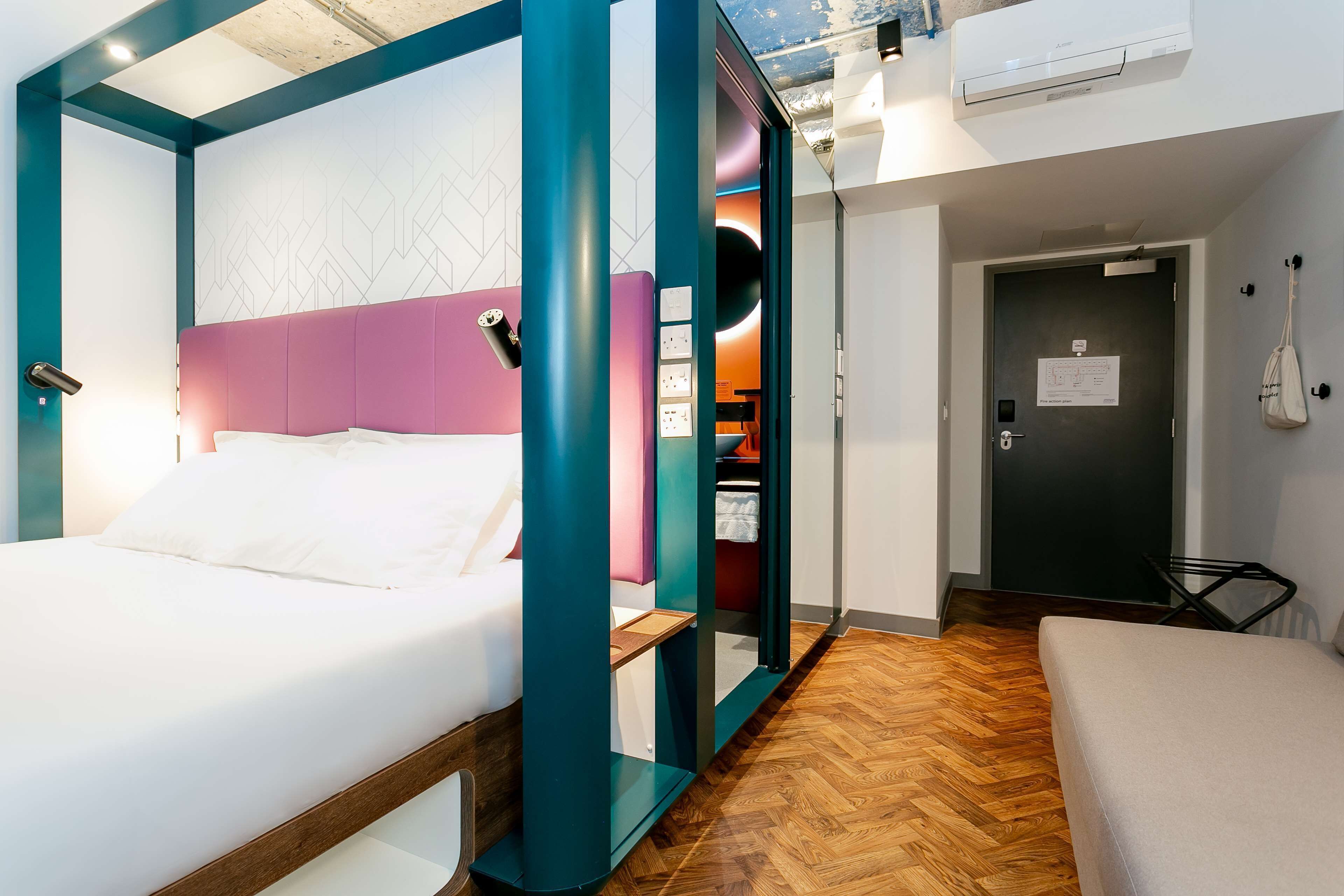 A modern hotel room with a bed, a desk, and a wardrobe.
