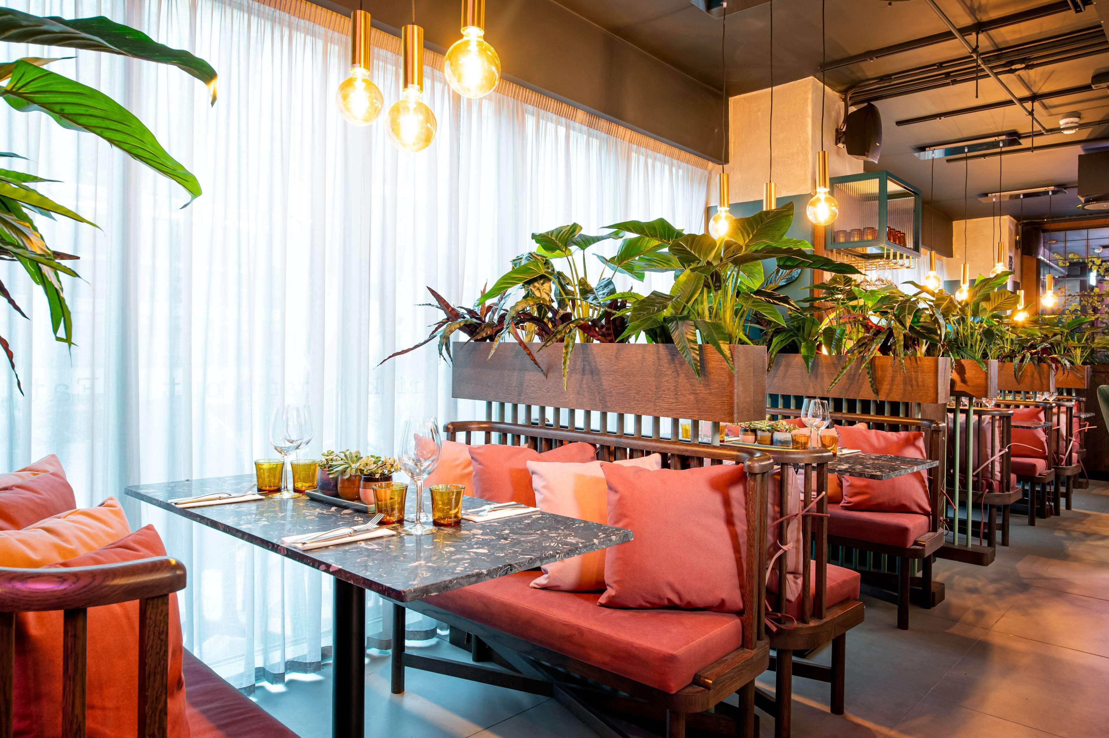 Un restaurante con mobiliario de madera, asientos acolchados e hiedra colgante.