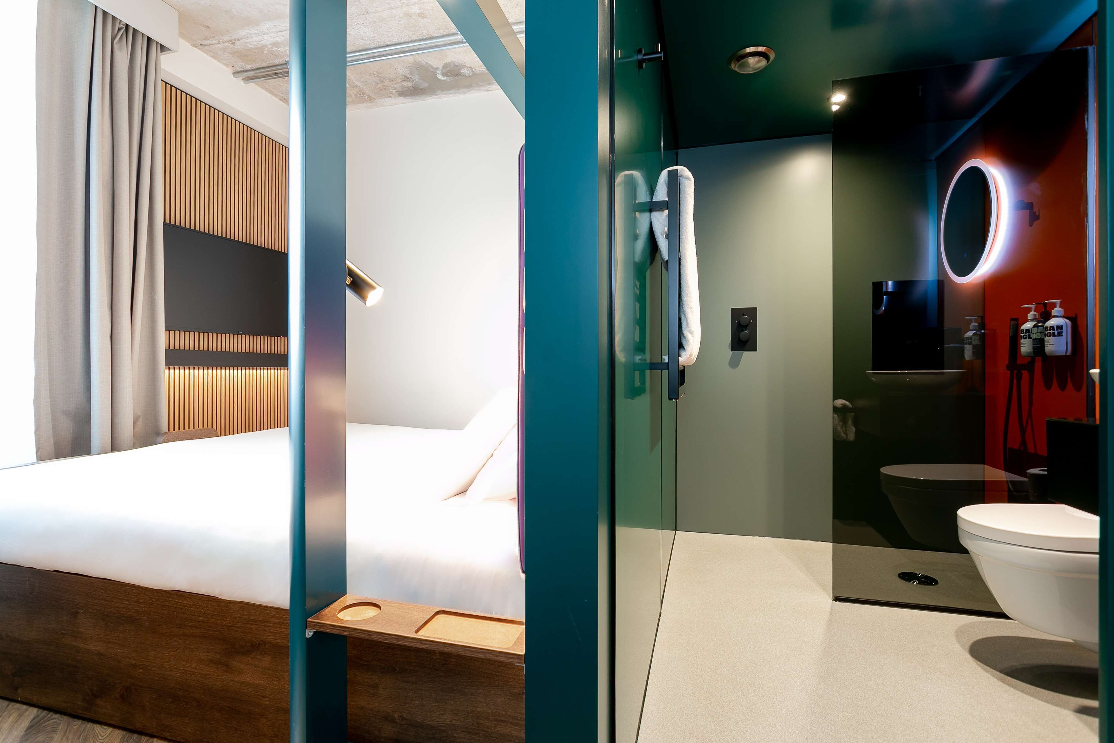 A modern hotel room with a bed, a glass-enclosed shower area, and a visible toilet.