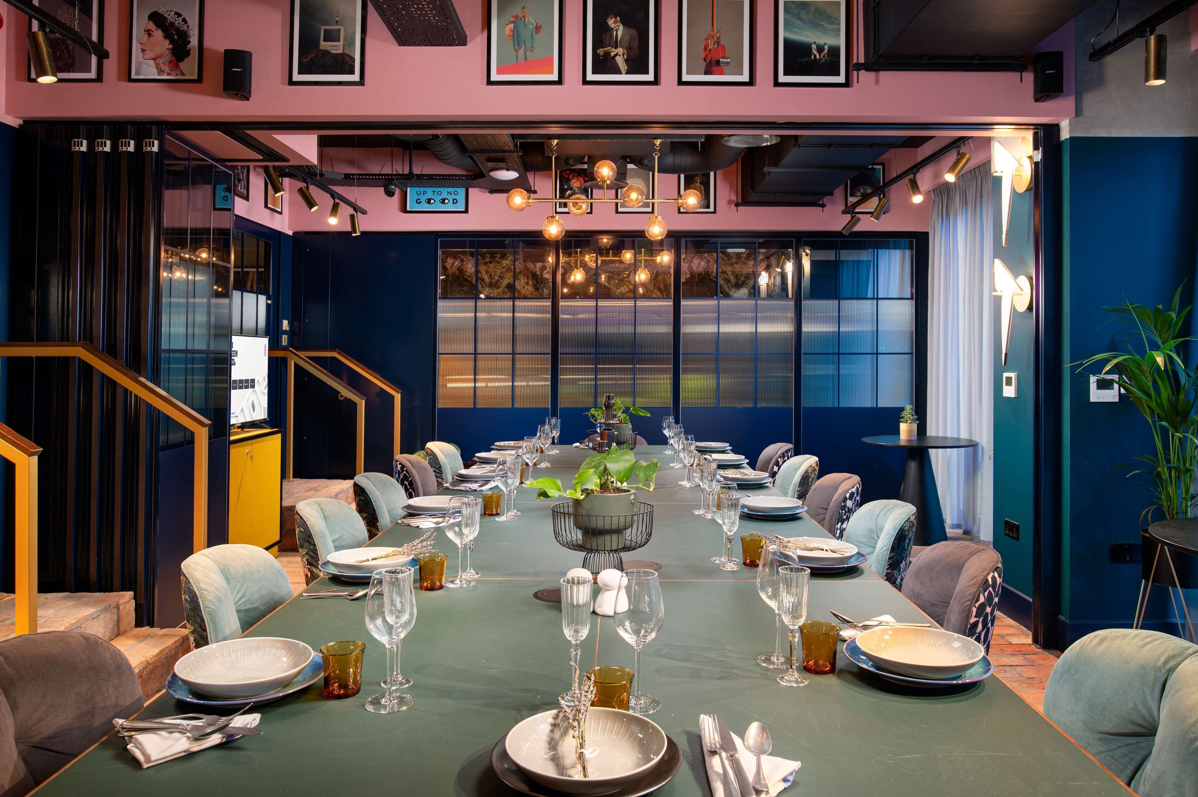 A dining area with a long table set for a meal, surrounded by chairs, and a central plant.