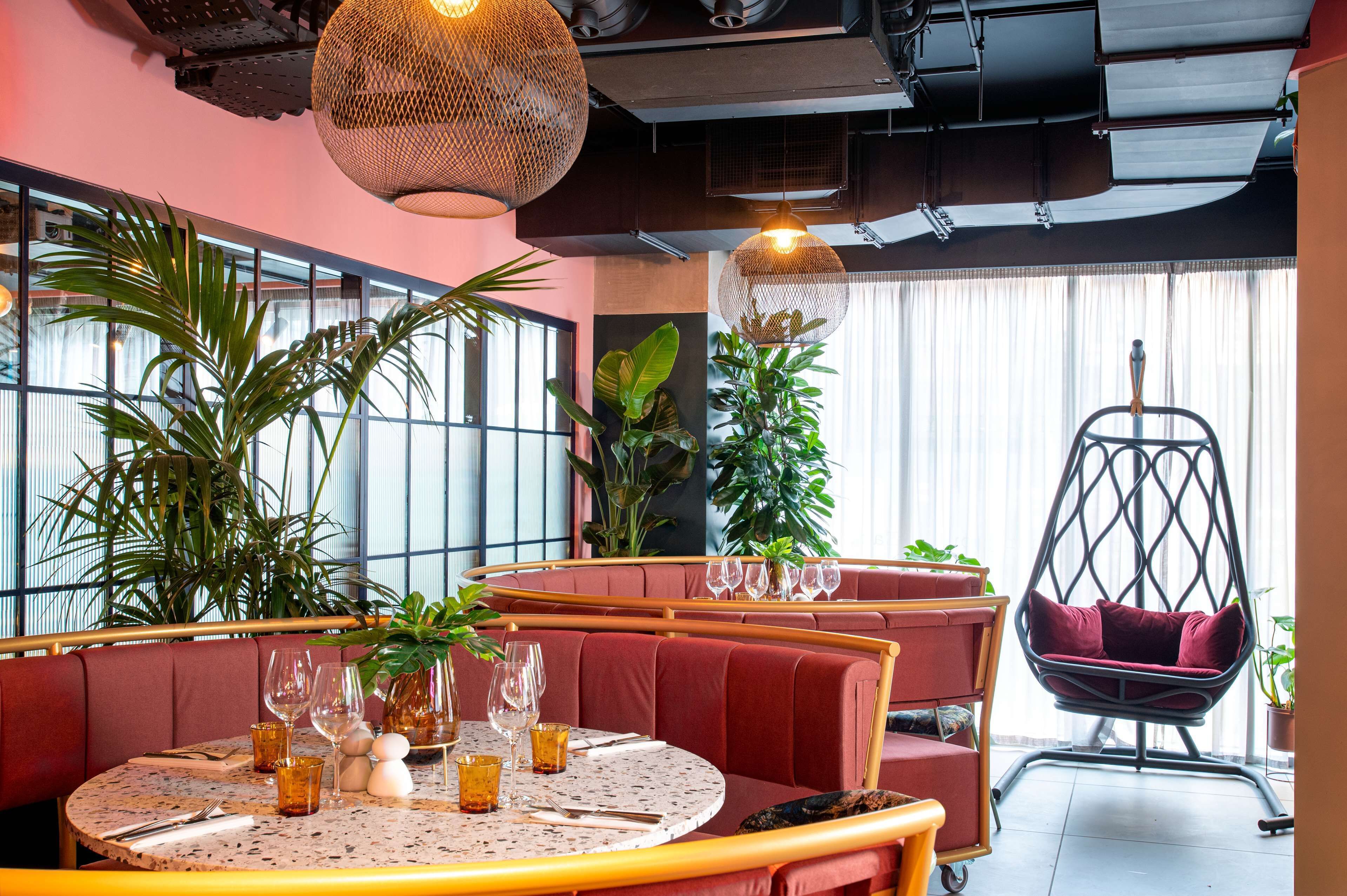 A restaurant with round tables, red cushioned booths, hanging wicker lamps, and potted plants.